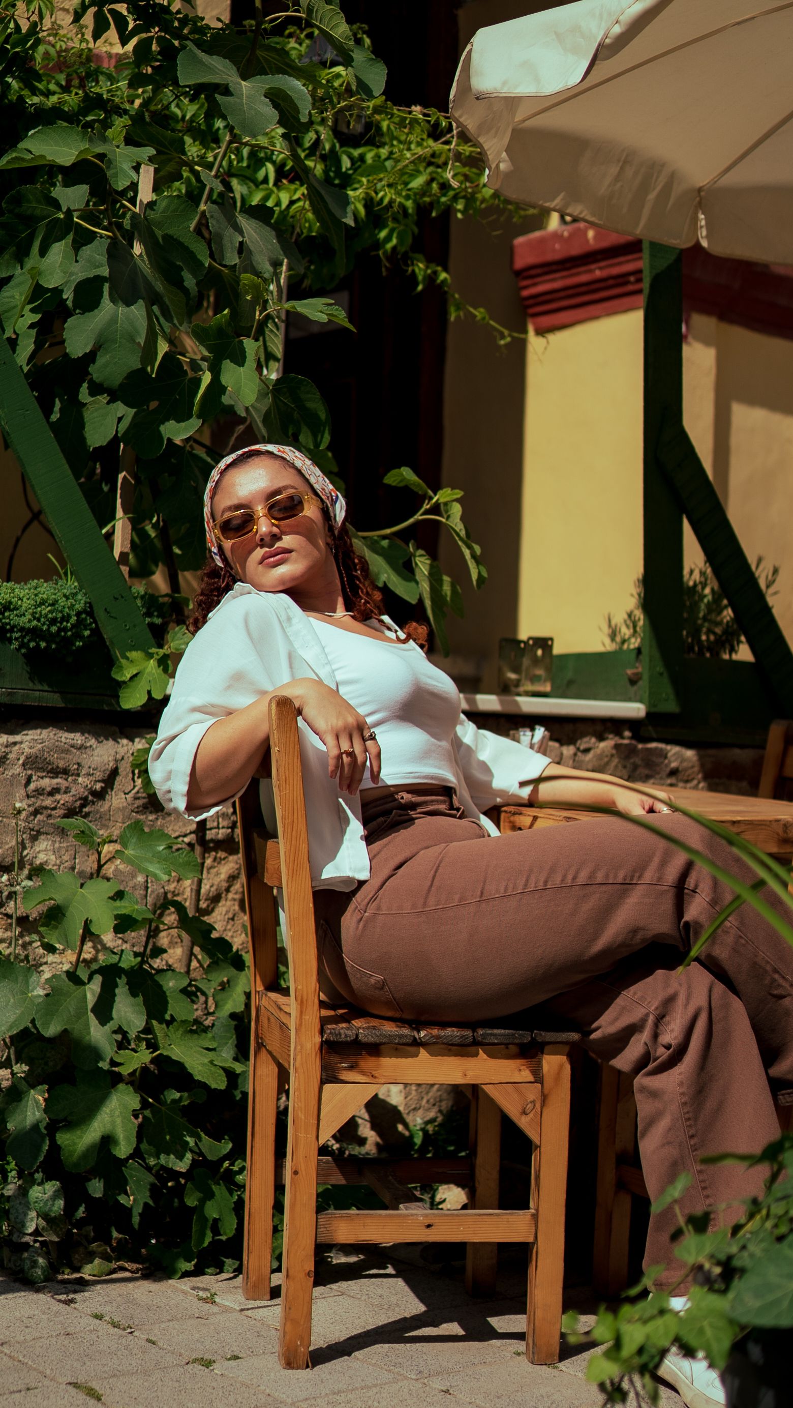 Caucasian woman in white shirt and headkerchief sitting on a chair enjoying the summer sun outdoors.
