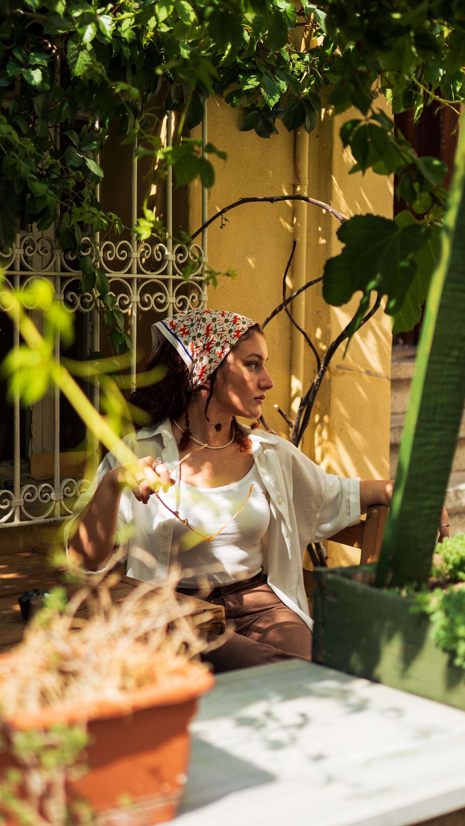 A woman wearing a headscarf relaxes on a sunny day in a garden setting.