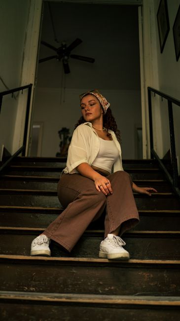 Young woman in brown wide-leg pants and white shirt sitting on staircase in vintage editorial style