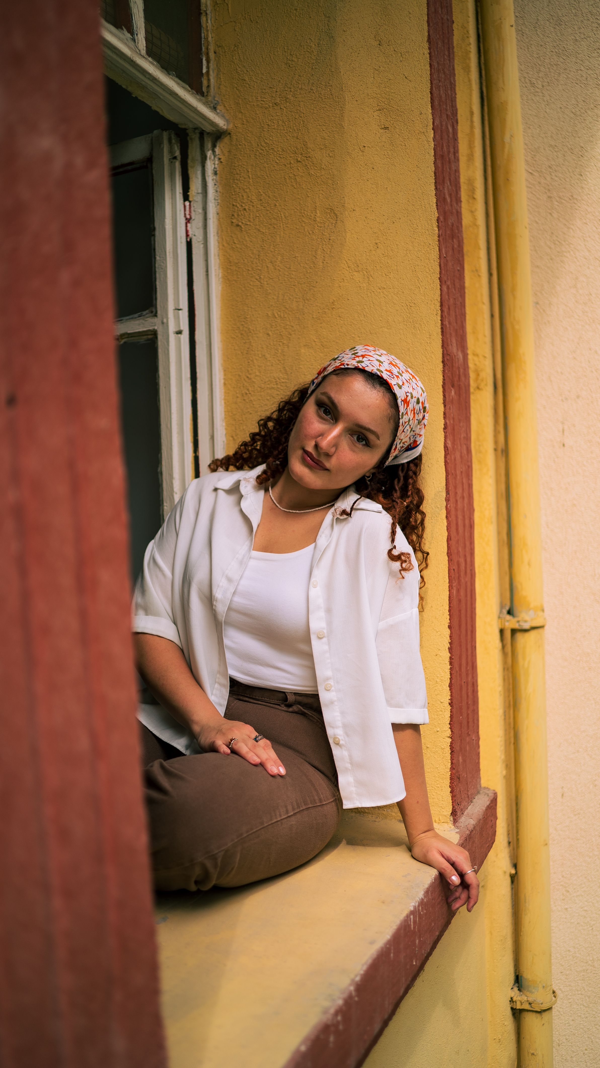 Woman with headscarf in summer clothing sitting on a window sill.
