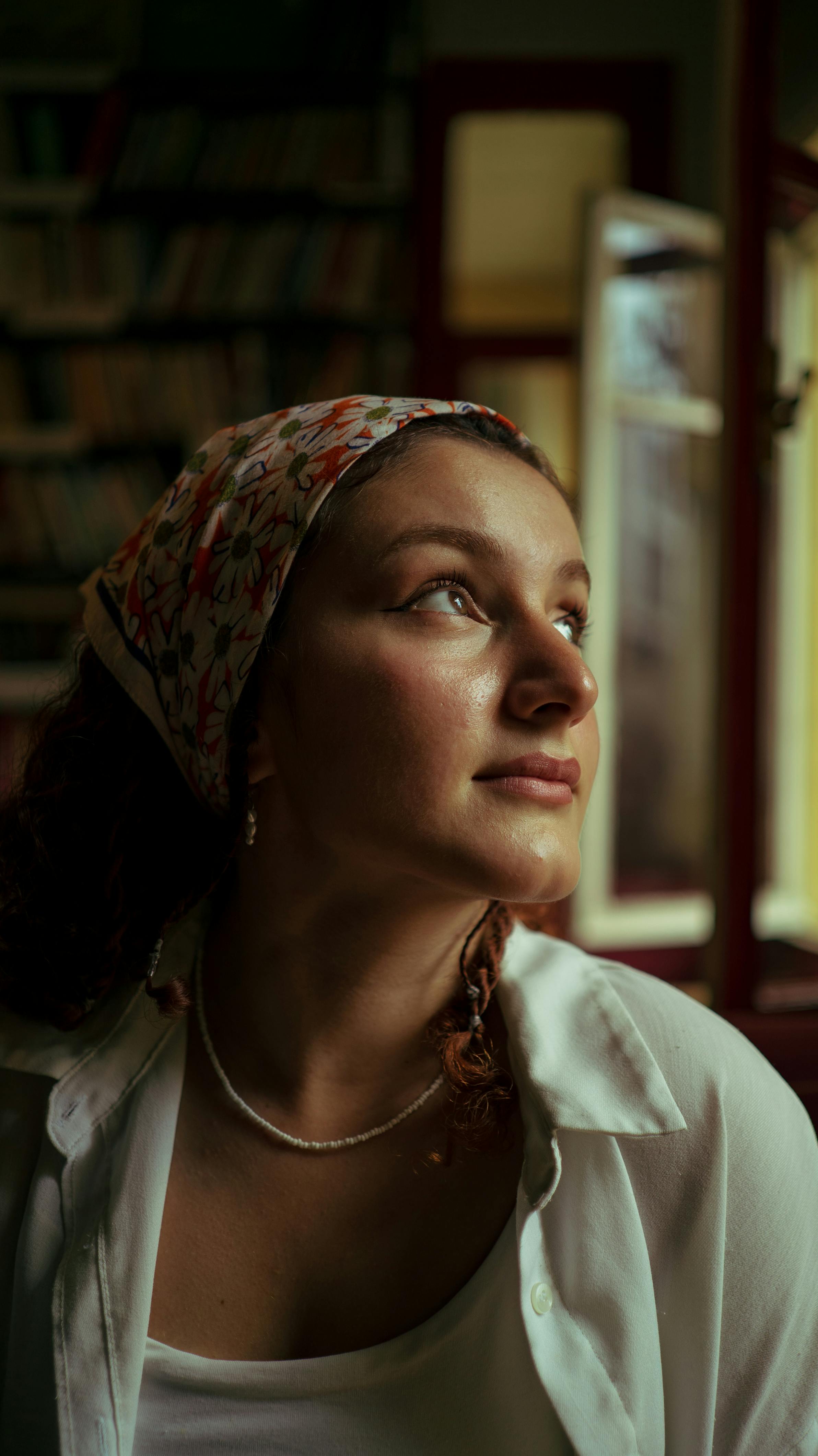 Portrait of a young woman with headkerchief gazing upwards indoors.