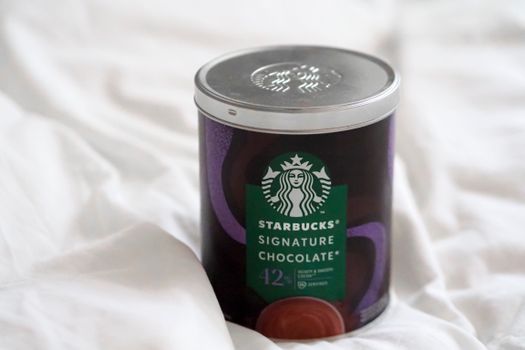 Close-up of Starbucks Signature Chocolate can on white fabric, offering premium taste.