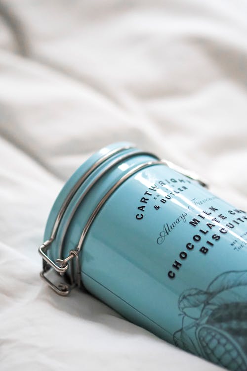 A blue canister on a bed with a white sheet