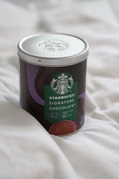 Starbucks chocolate tin on white bed sheets, perfect for cozy product displays.
