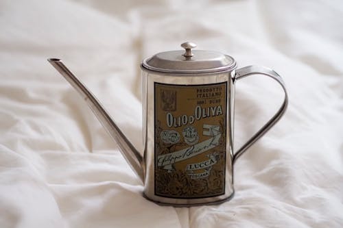 A silver watering can on a bed with a white sheet