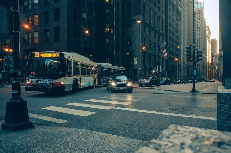 City bus and cars navigate a downtown intersection at twilight, urban USA setting.