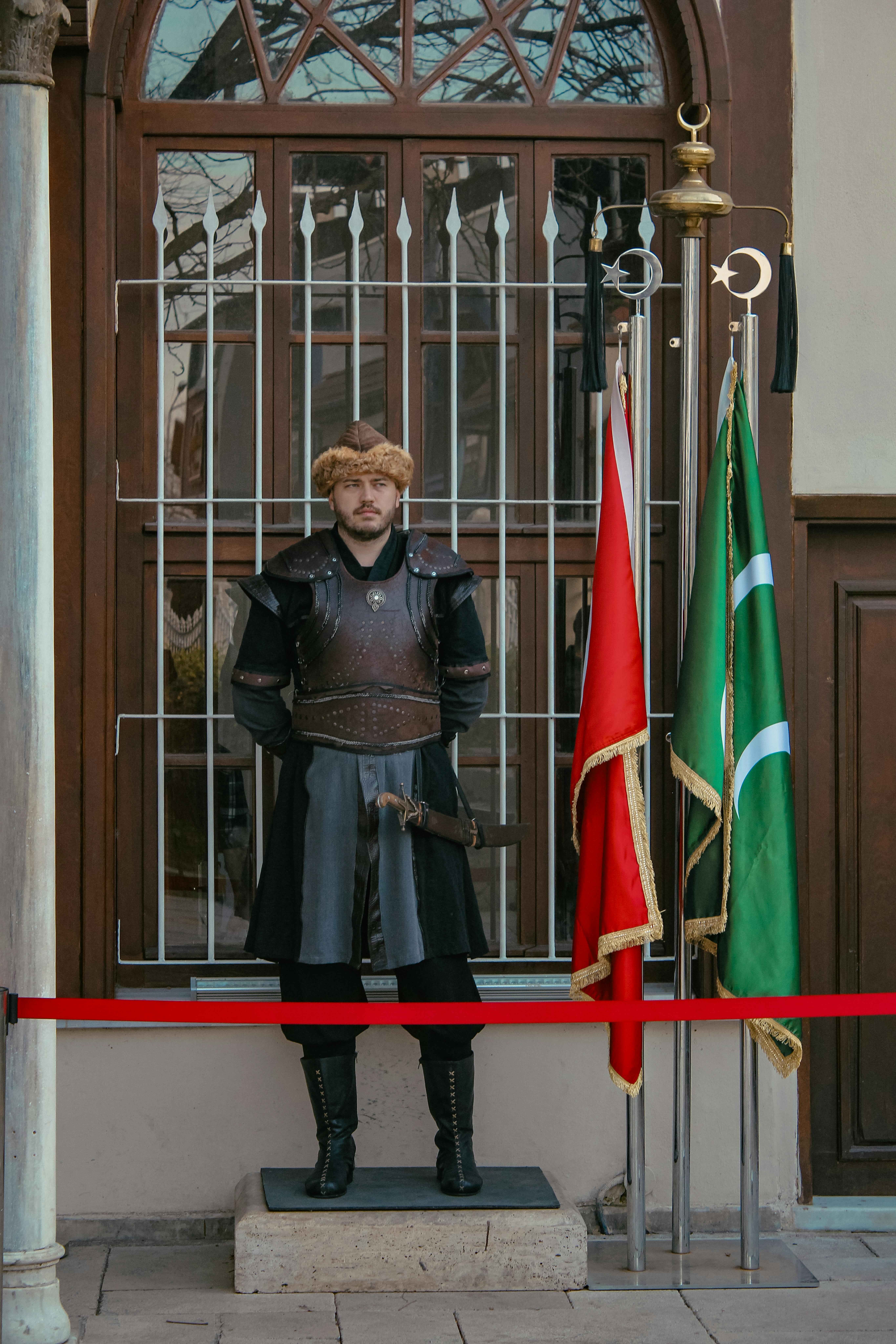 A man in traditional armor stands guard outside a museum in Bursa, Türkiye, showcasing medieval attire.