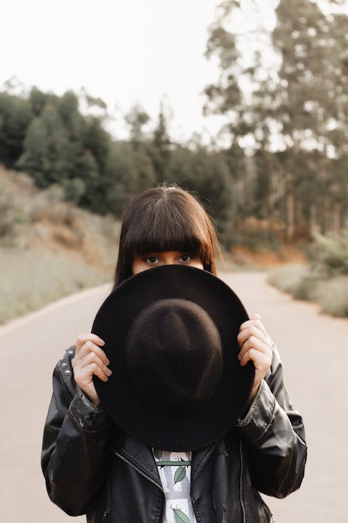 Foto De Enfoque Selectivo De Una Mujer Parada En Medio De Una Carretera Mientras Se Cubre Parte De La Cara Con Un Sombrero Fedora