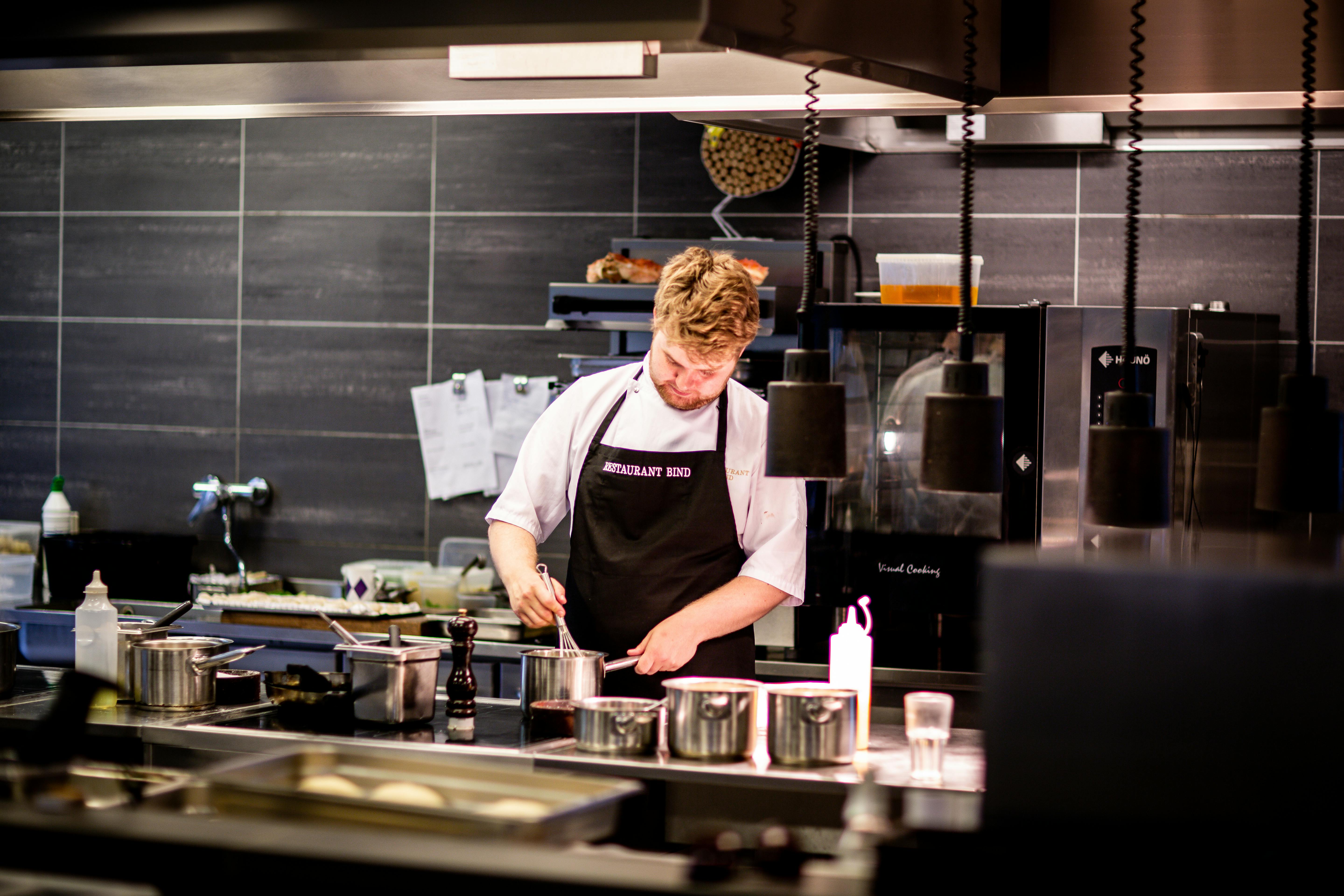 Chef Cocinando En La Cocina Retrato De Un Joven Apuesto Con Un Delantal  Negro Y Un Delantal Cocinando Comida En El Restaurante Fotos, retratos,  imágenes y fotografía de archivo libres de derecho.