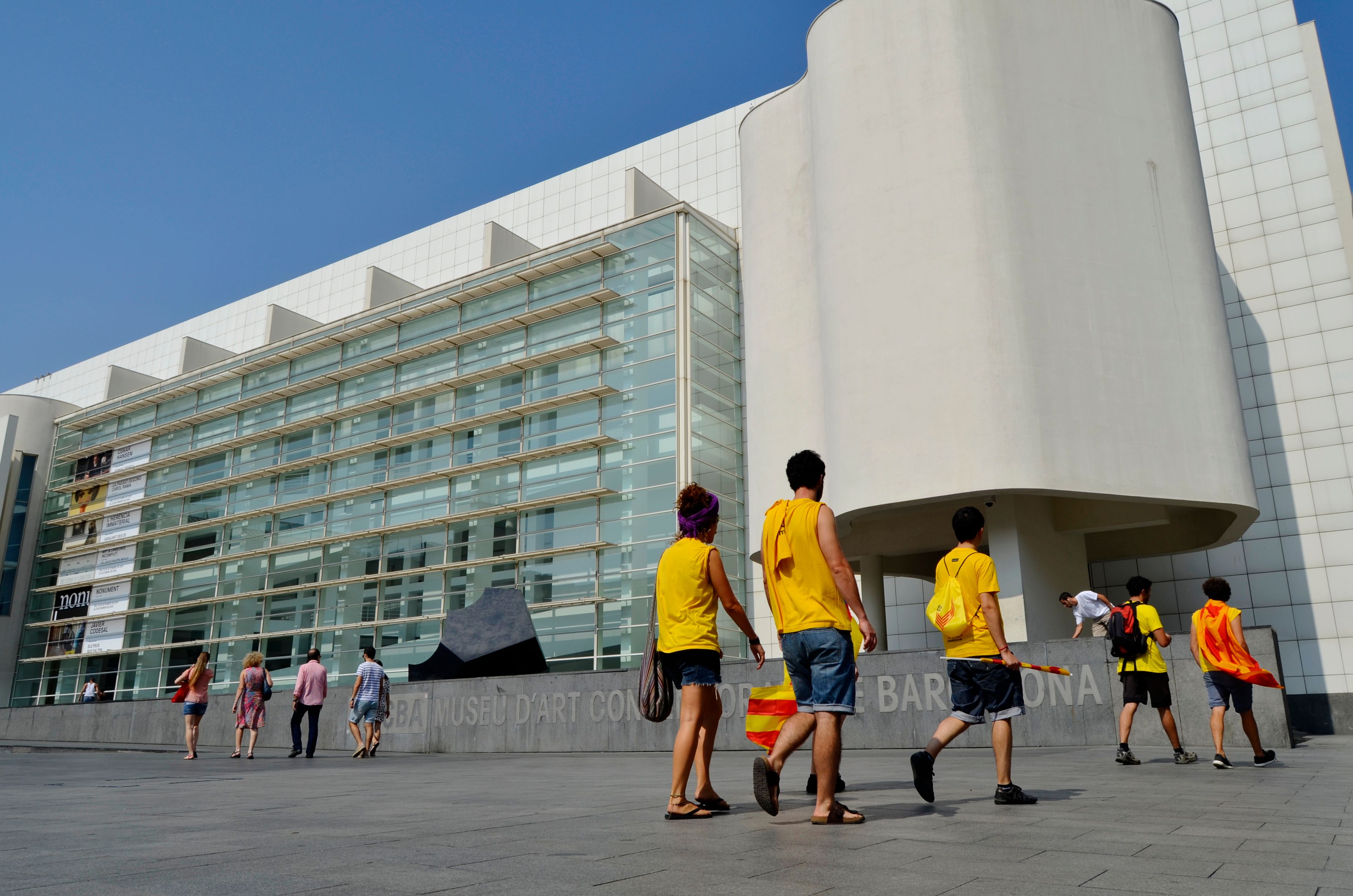 Tourists walk by the contemporary MACBA museum in Barcelona, Spain, showcasing modern architecture.