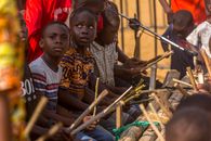 A group of children performing traditional music with wooden instruments outdoors.