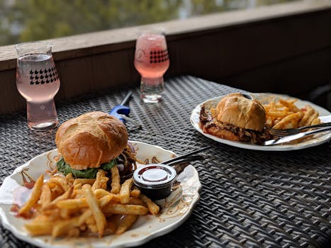 Tasty burgers with fries and pink beverages on an outdoor table setting.