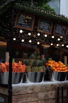 Colorful market stall in England showcasing fresh fruits and vegetables under festive lights.