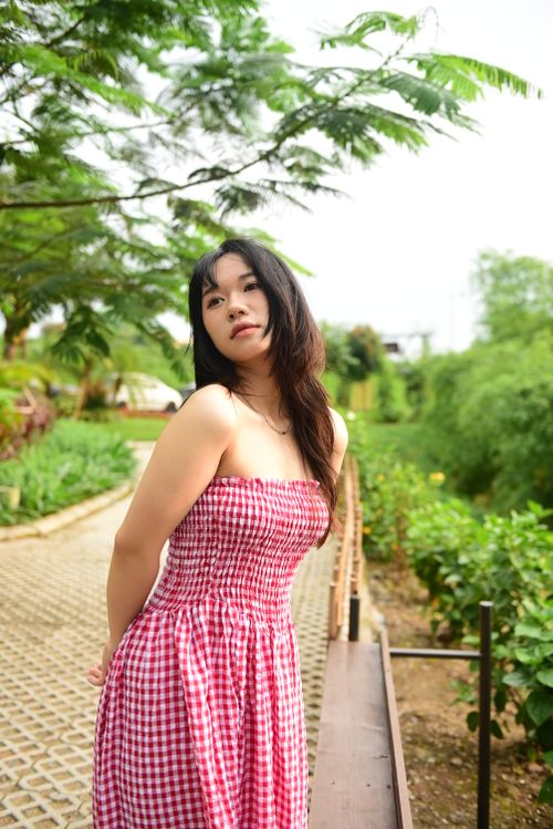 Free Asian woman in a red dress posing in a vibrant park. Stock Photo