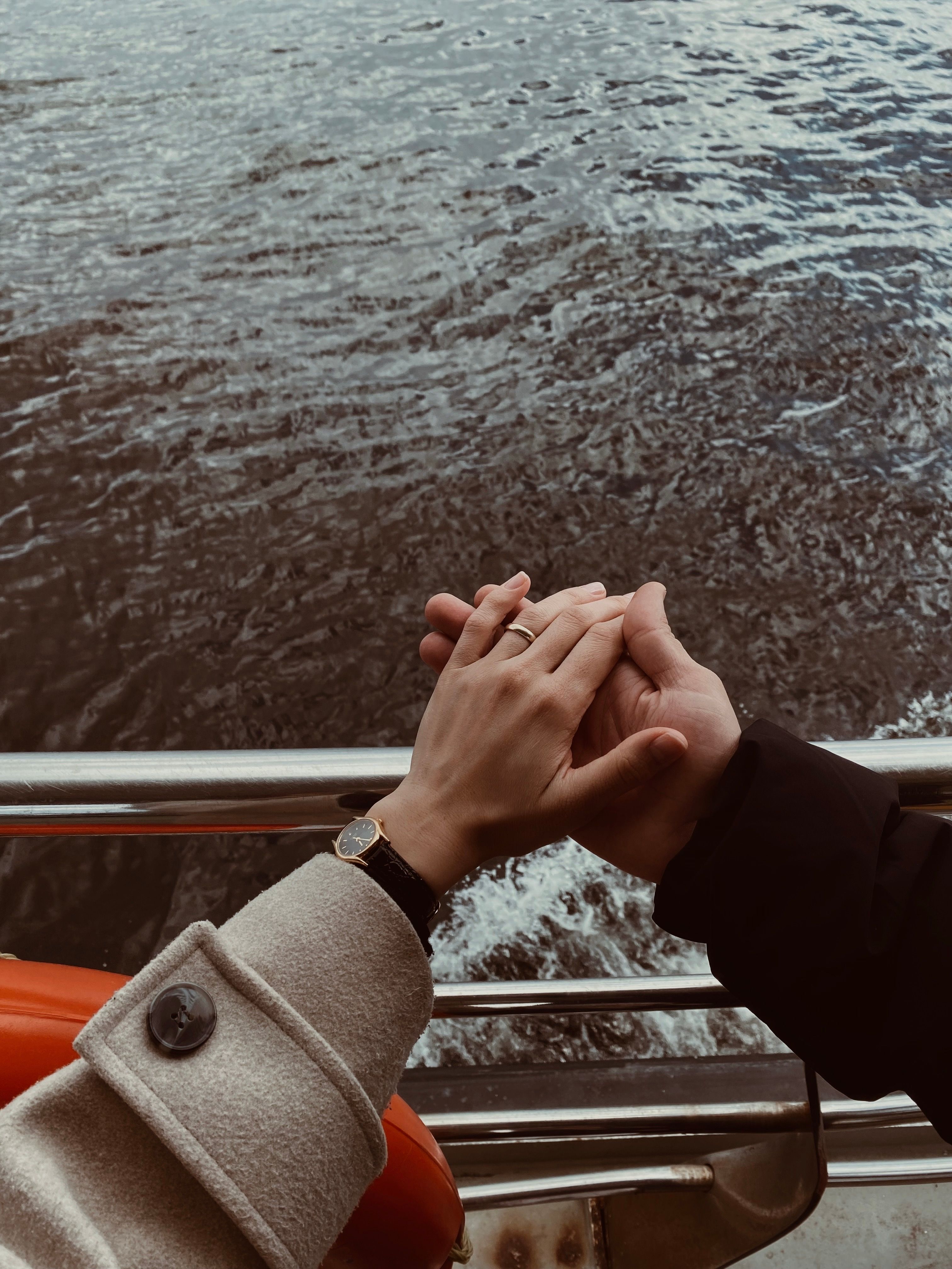 A romantic shot of a couple holding hands on a boat, with a serene sea backdrop.