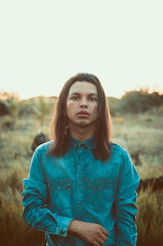 日落时分，一名穿着牛仔衬衫的年轻人在户外留下肖像，背景是自然风光