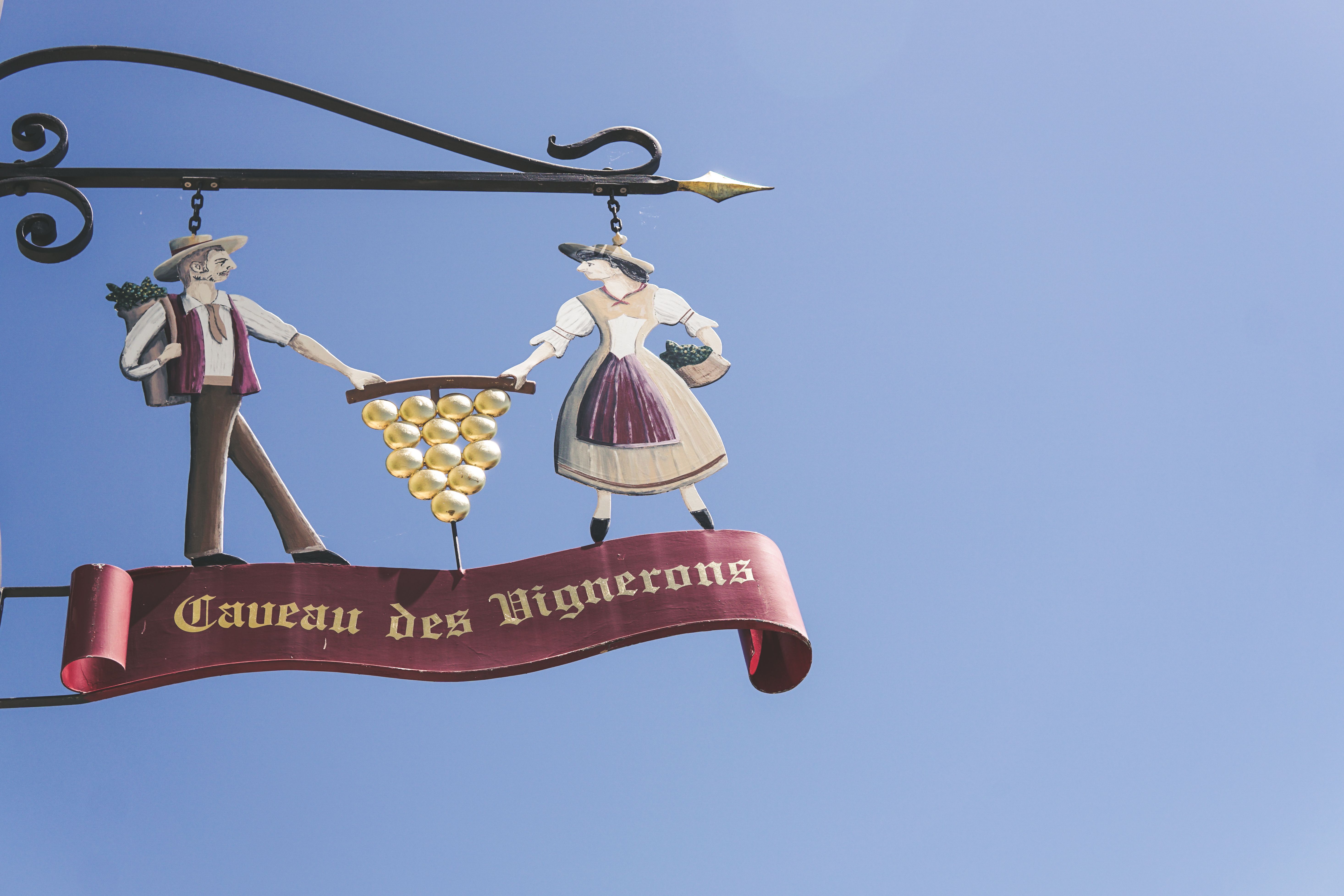 Decorative wine-themed sign 'Caveau des Vignerons' against a clear blue sky.