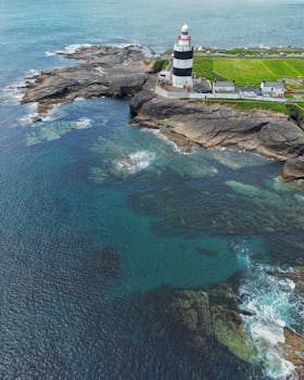 Aerial view of Hook Lighthouse, a landmark on the Irish coast, surrounded by rocky sea shores.