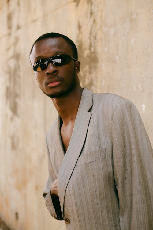 A man in a suit and sunglasses standing against a wall