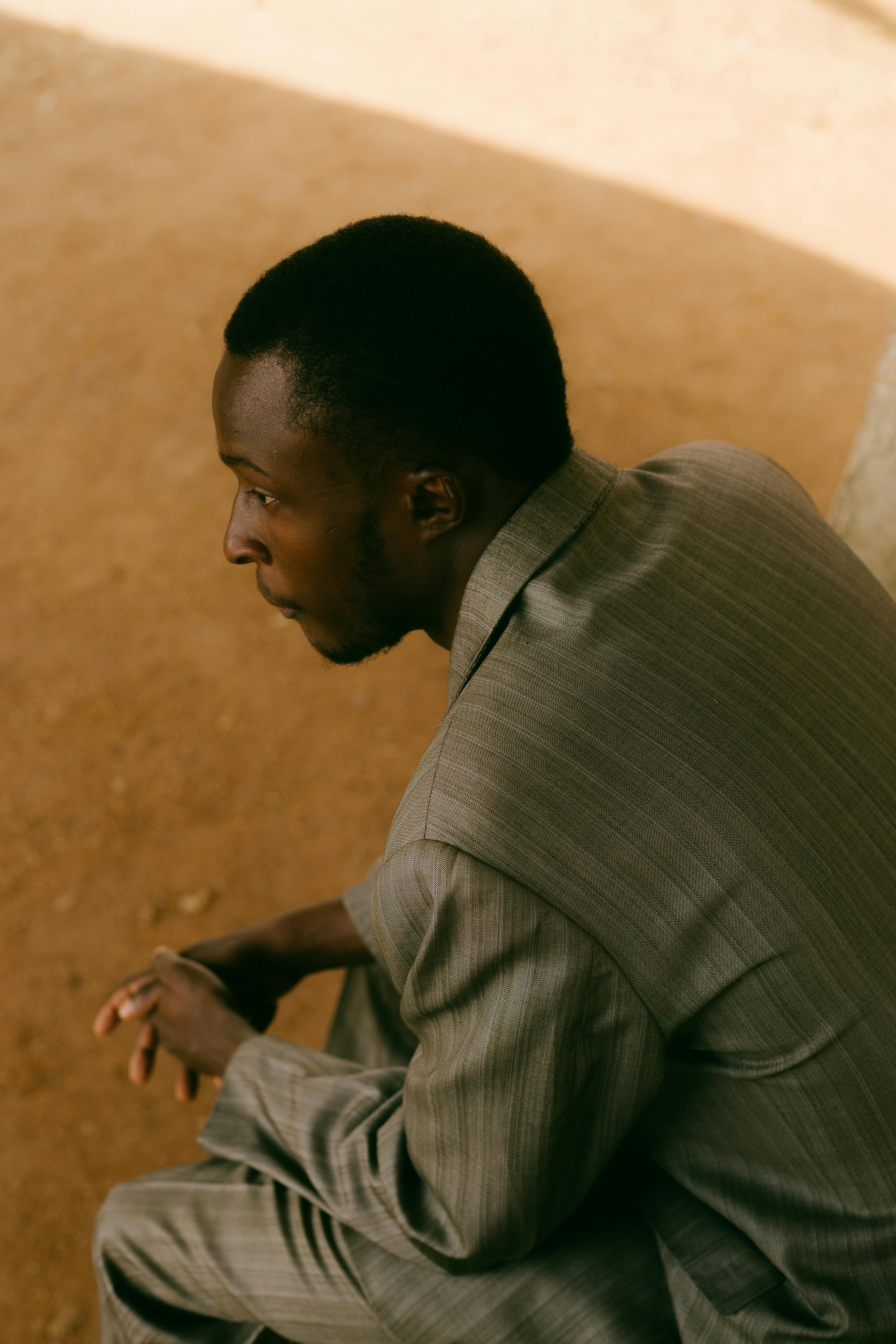 Side view of a man in a gray suit sitting on a sandy surface, deep in thought.