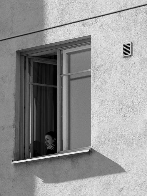 A black and white photo of a person looking out of a window