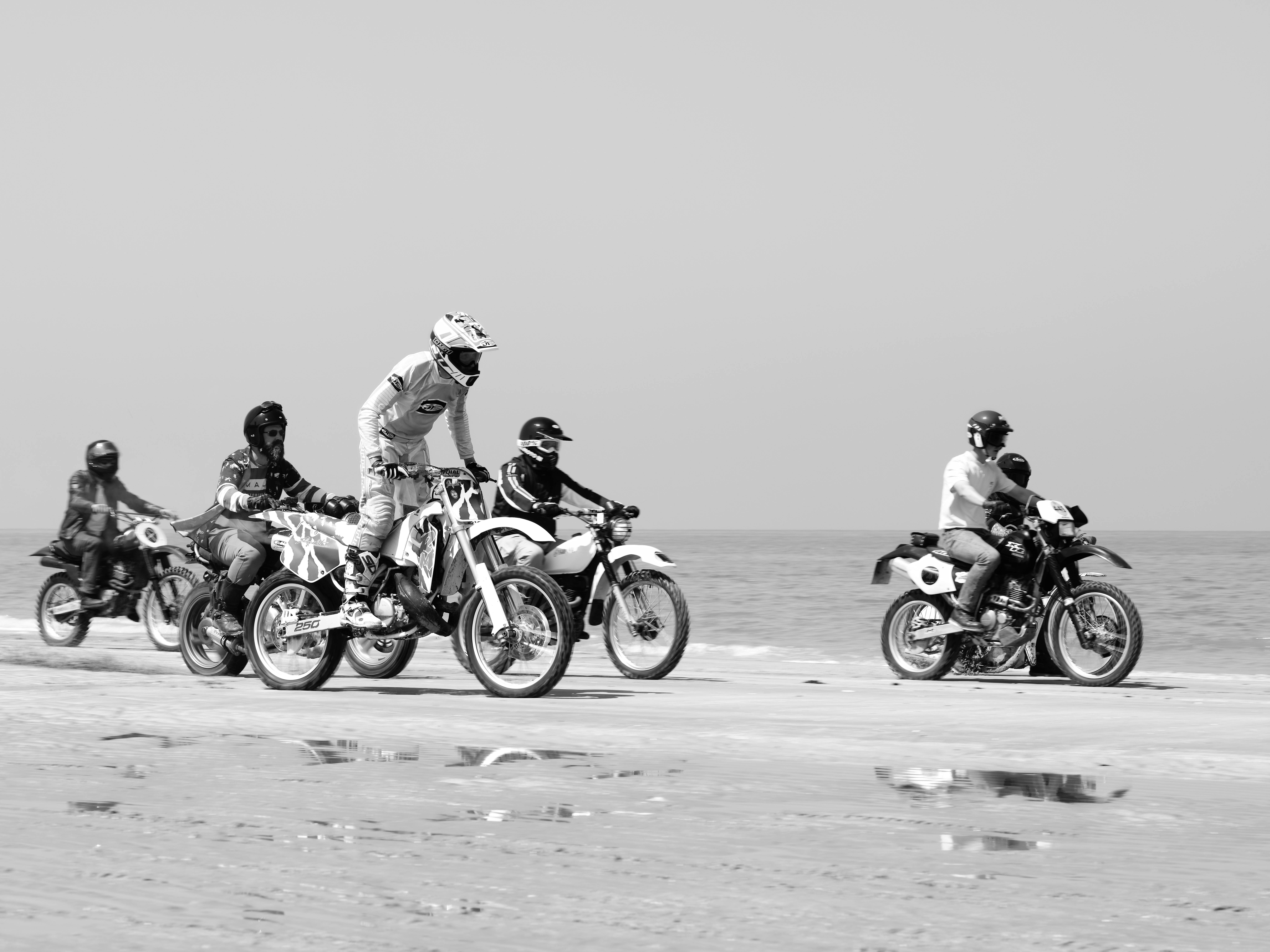 Group of motorcyclists racing on Margate Beach in black and white, showcasing thrill and adventure.