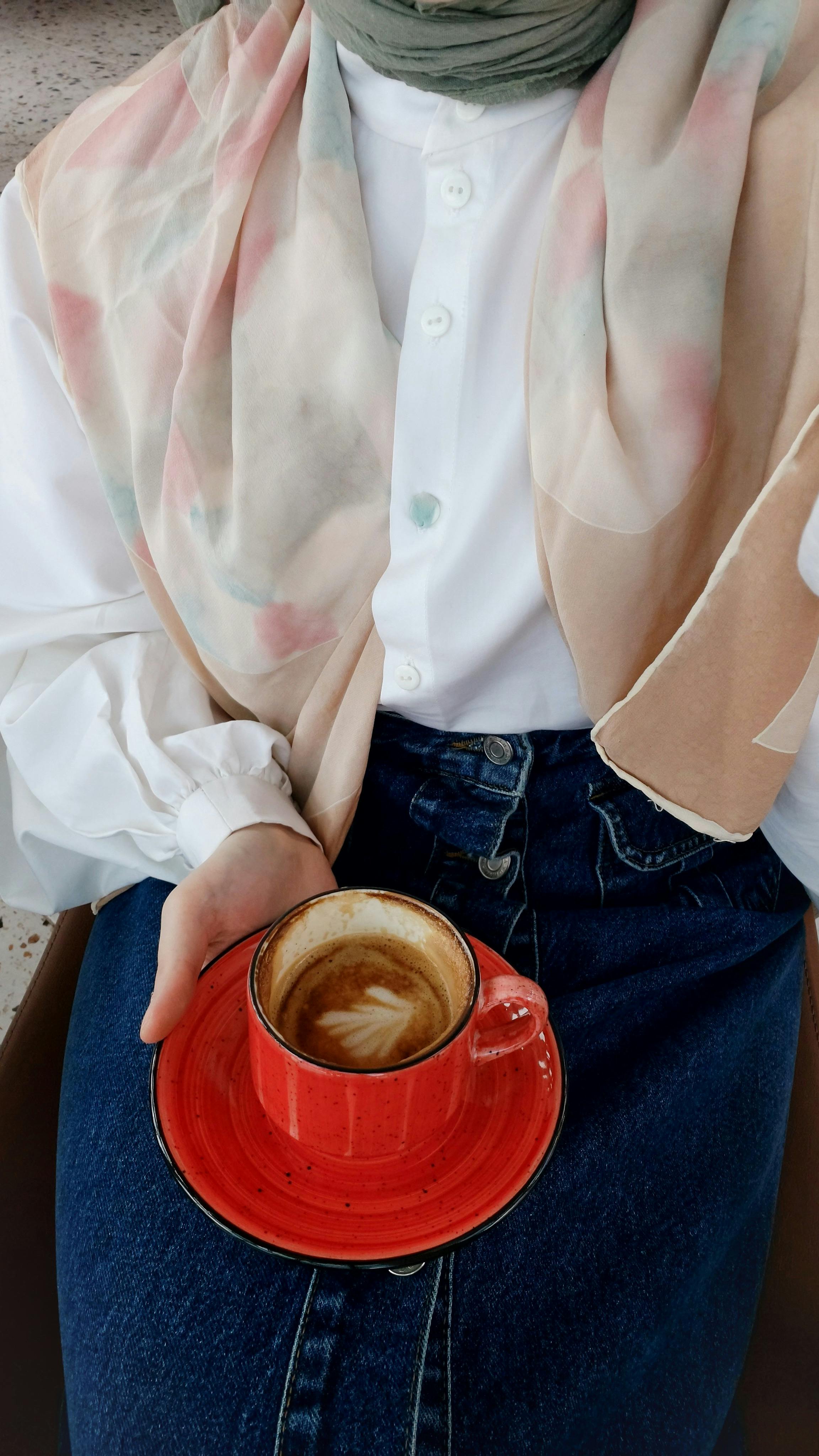 Chic fashion ensemble of denim, blouse, scarf, and coffee cup.