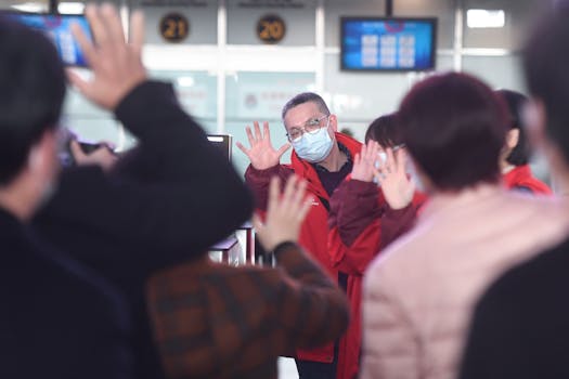 Group of travelers wearing face masks waving goodbye at a busy airport terminal.