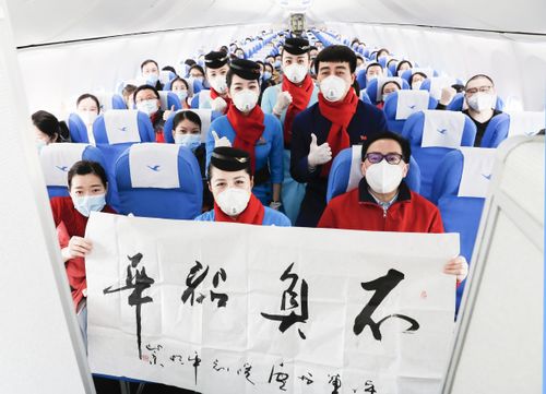 Free Airline crew and passengers wearing masks on an aircraft, holding a sign with Chinese characters. Stock Photo