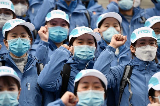 Group of healthcare workers wearing masks and blue uniforms holding fists up, showing unity and strength.
