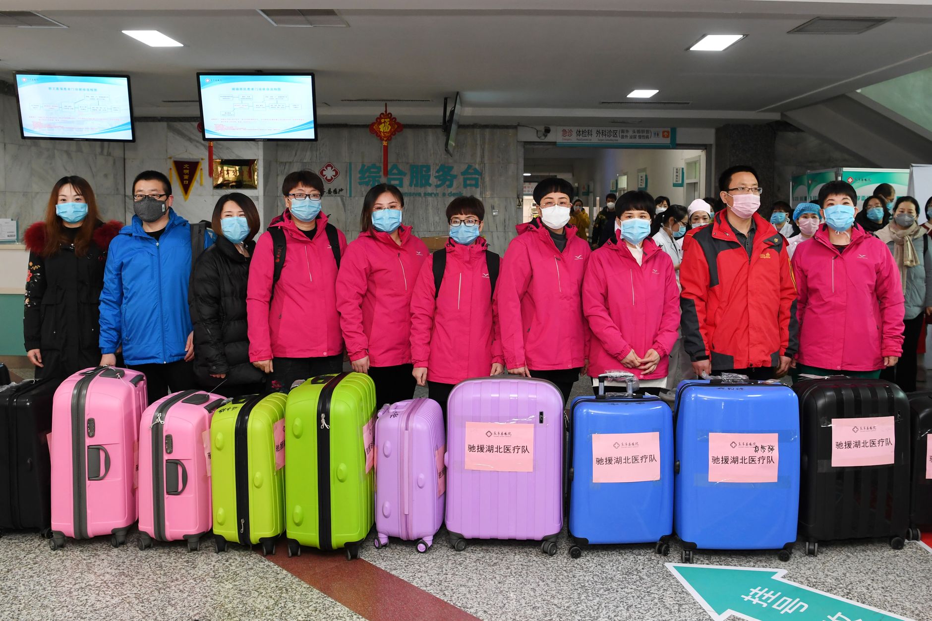 A group of people wearing masks standing with colorful luggage at an airport terminal.