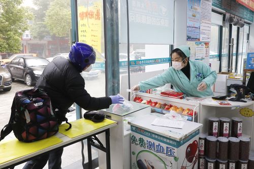 Free Customer purchasing items at a store counter in Wuhan, both wearing face masks for safety. Stock Photo