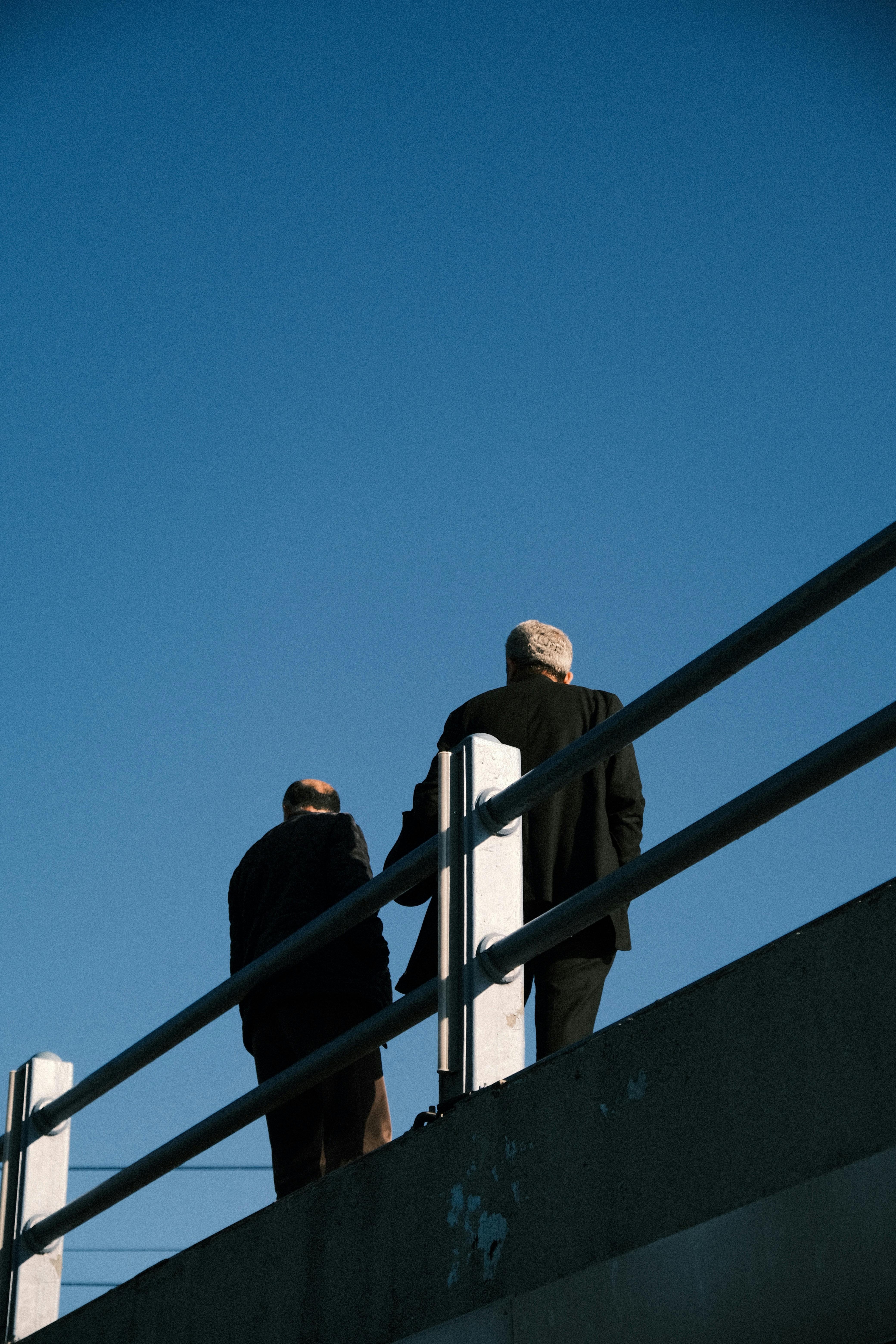 Silhouette of two men standing on a bridge with a clear blue sky as the backdrop, captured from a low angle.