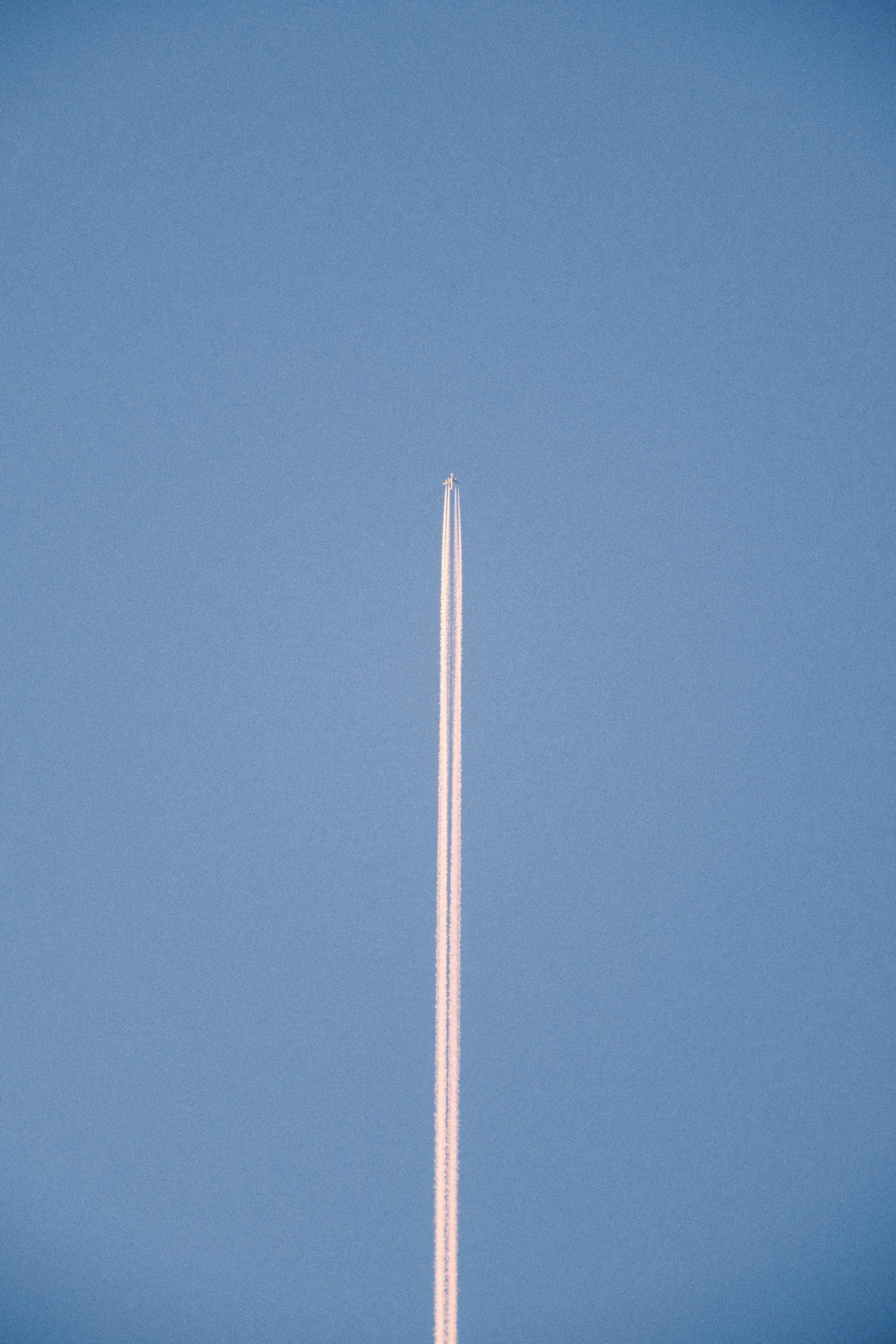 Vertical shot of a distant airplane leaving a contrail in a clear blue sky.