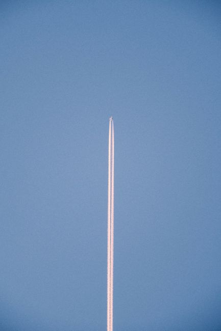 Vertical shot of a distant airplane leaving a contrail in a clear blue sky.