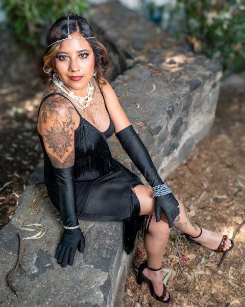 A woman in a black dress and gloves sitting on a rock