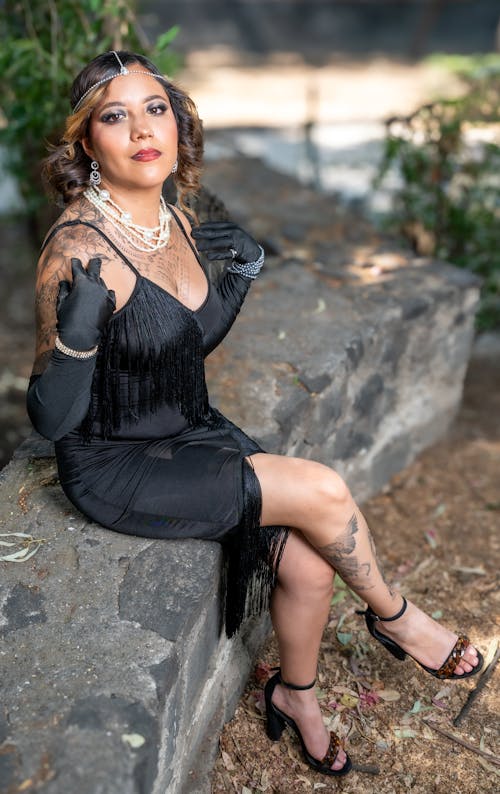 A woman in a black dress and black gloves sitting on a rock