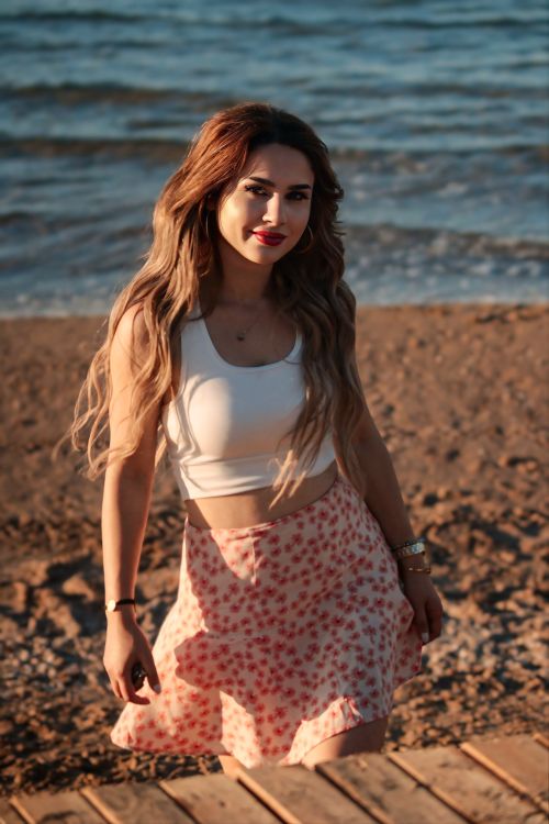 Free A woman smiling on a sandy beach during sunset, wearing casual attire. Stock Photo