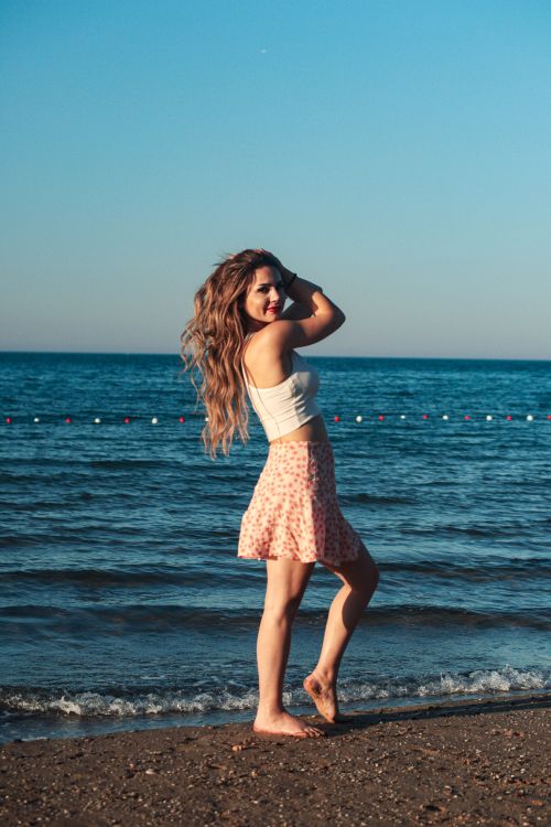 Free Woman in summer outfit enjoying a sunny day at the beach. Perfect for lifestyle and fashion themes. Stock Photo
