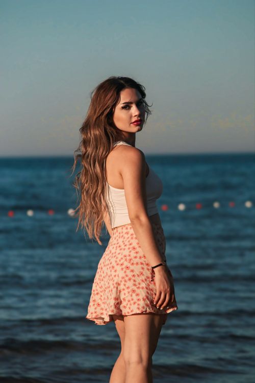 Free Stylish woman in floral skirt and tank top by the ocean at sunset. Stock Photo
