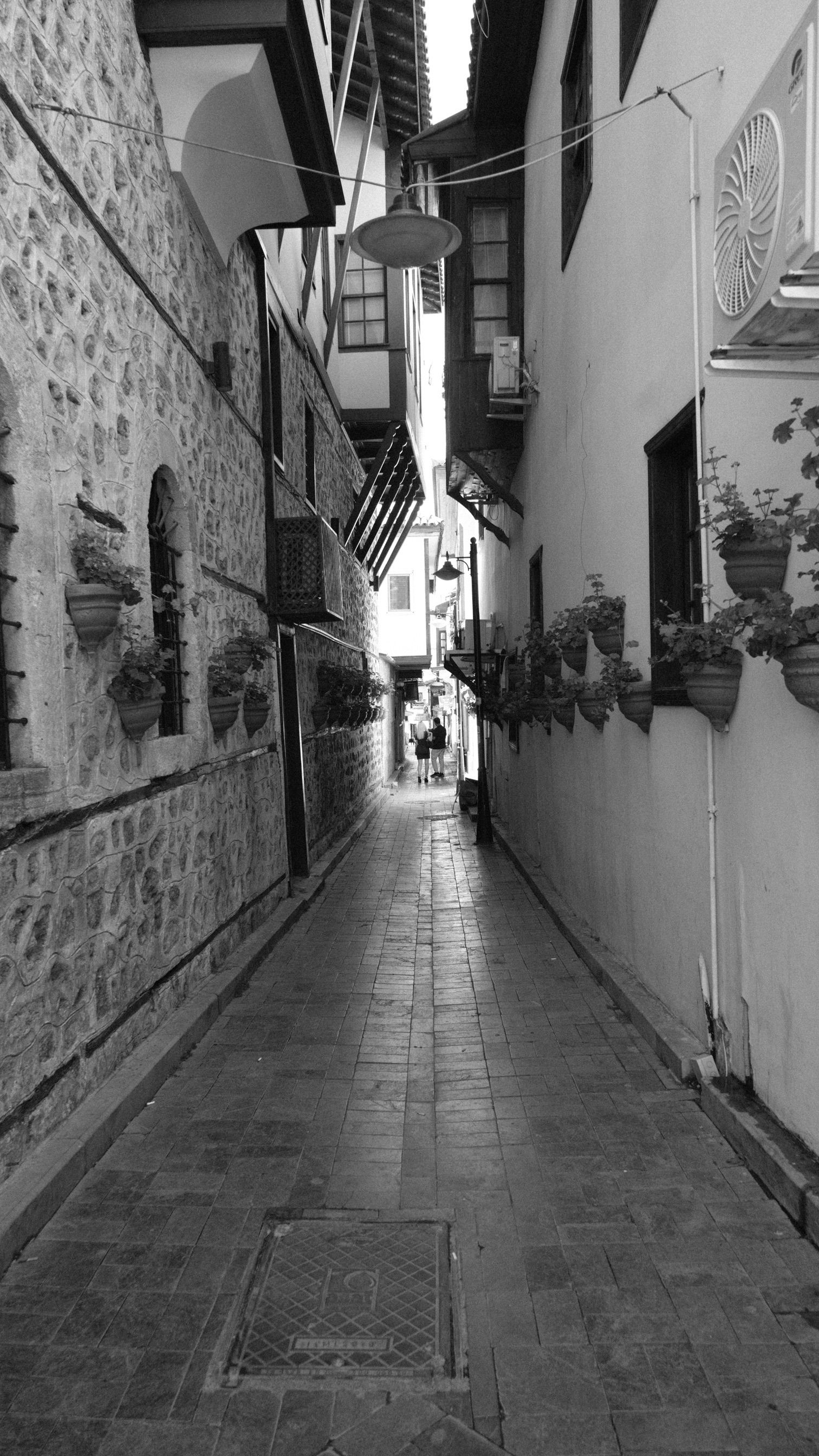 Charming narrow alley with flower pots, showcasing Antalya's historic architecture.