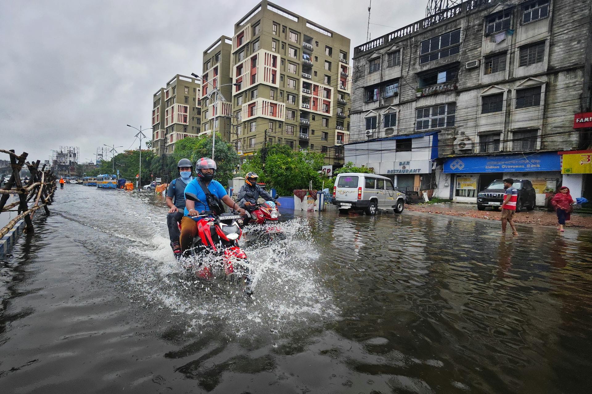 Bikers navigating through flooded streets in Kolkata, India amidst urban rainfall.