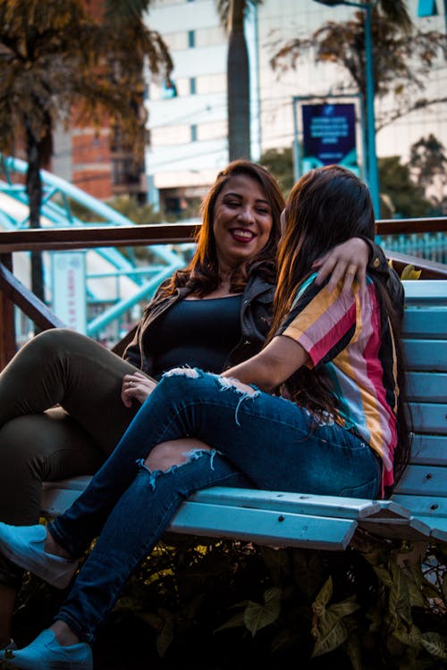 Two Women Sitting on White Wooden Bench