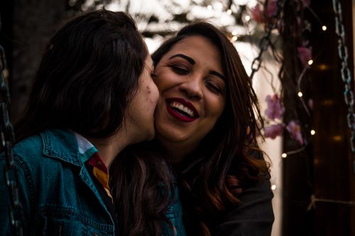 Free Happy LGBTQ couple smiling and enjoying a close moment outdoors, featuring colorful lights. Stock Photo