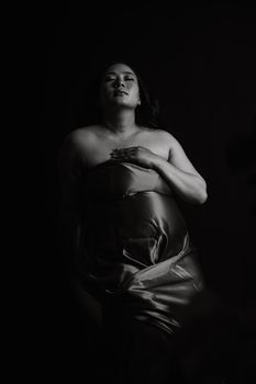 Artistic black and white portrait of a pregnant woman in a studio setting.