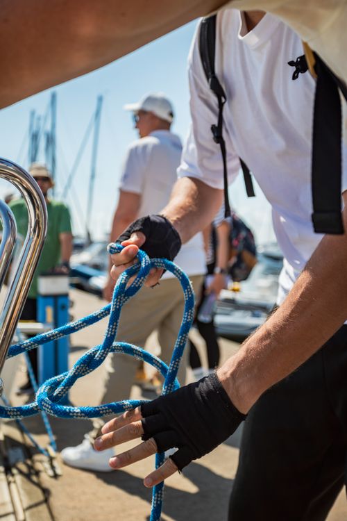 Free Close-up of hands tying a rope knot at a busy harbor pier on a sunny day. Stock Photo