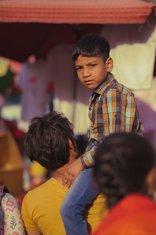 Free A father carrying his son on his shoulders in a vibrant, crowded street market. Stock Photo