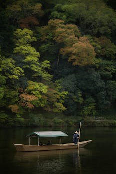 A serene scene in Kyoto with a boatman guiding a wooden boat on a calm river against colorful autumn trees.