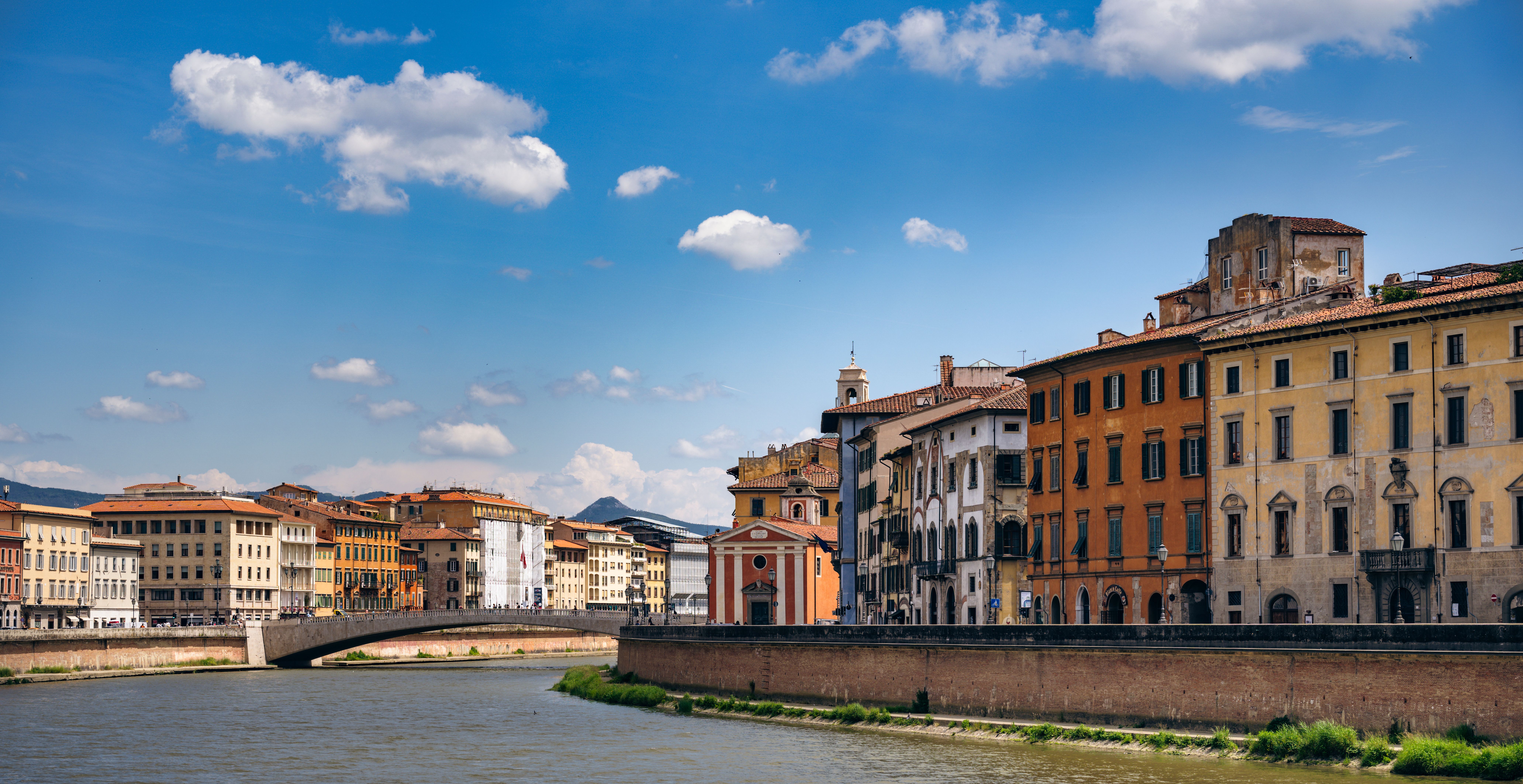 Charming view of Pisa's riverside with historic, colorful buildings under a bright blue sky.