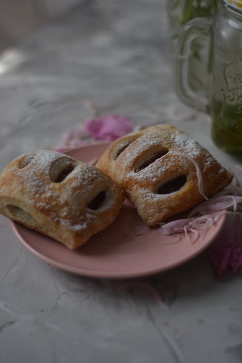 Two pastries on a pink plate with a jar of jam